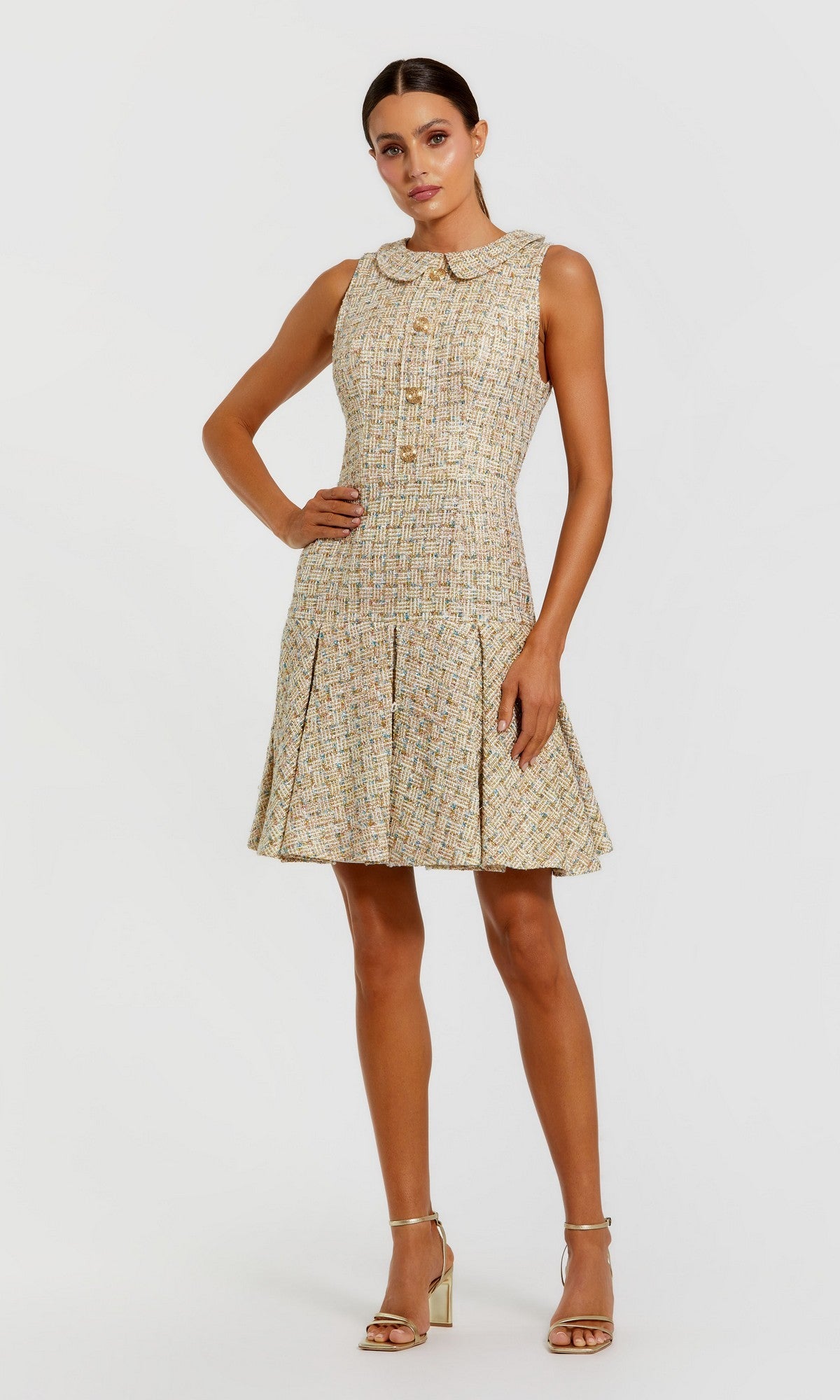 Woman wearing the Mac Duggal 21068 Short Party Dress in Gold Multi, featuring a sleeveless design, peter pan collar, front buttons, and pleated skirt, posing in heels against a plain white background.